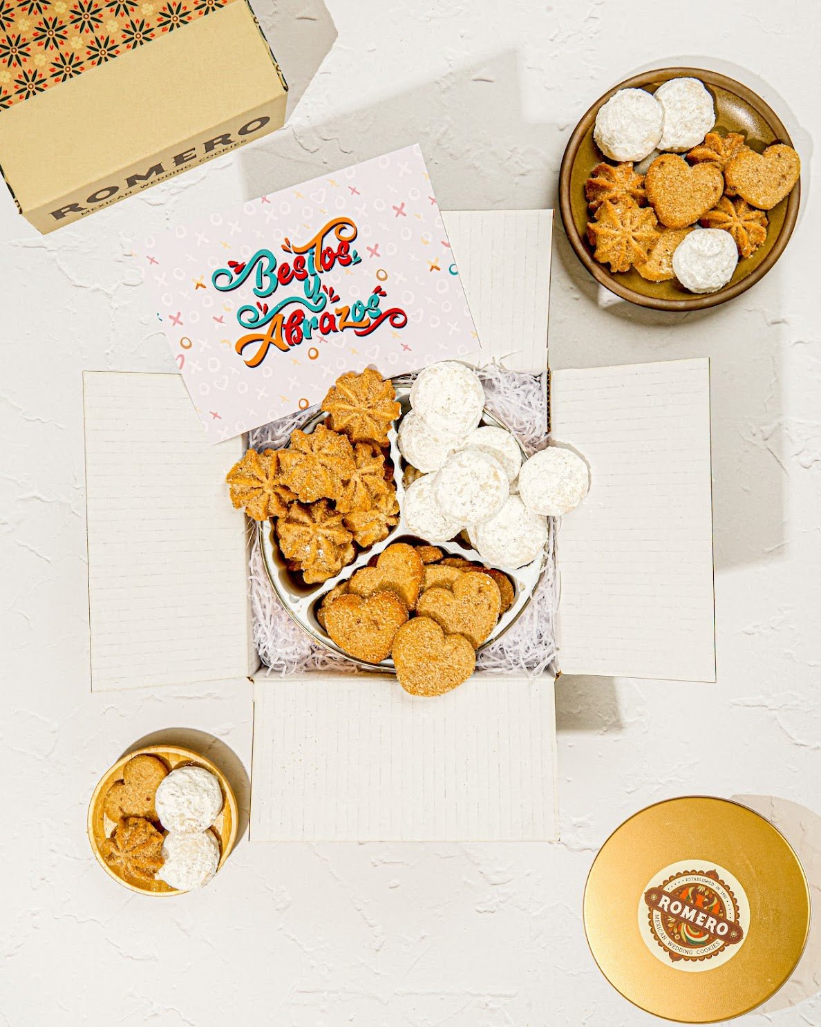 open cookie tin in a box with a 'love' card and cookies around the box with white background