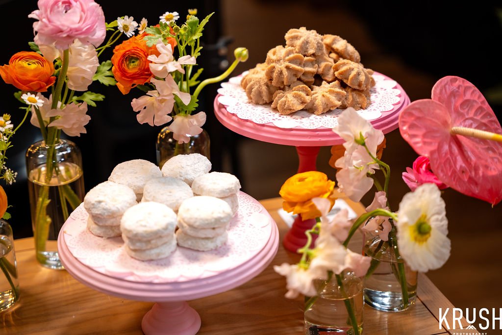 mexican cookies on pink stands with floral decorations on a wooden table.