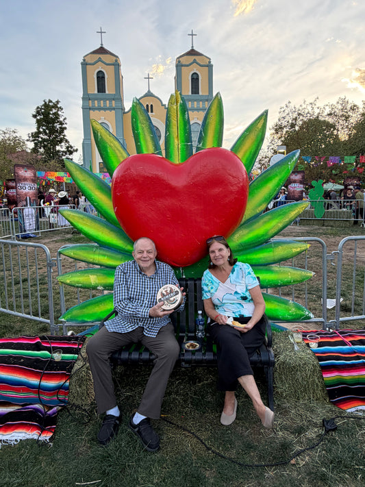 older couple in front of brightly colored heart holding mexican cookie tin
