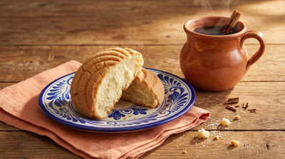 Mexican concha sweet bread broken in half on a Talavera ceramic plate with a steaming cup of cafe de olla coffee