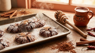 Mexican hot chocolate cookies — dark chocolate crinkle cookies dusted with powdered sugar on a baking sheet with molinillo whisk and cocoa