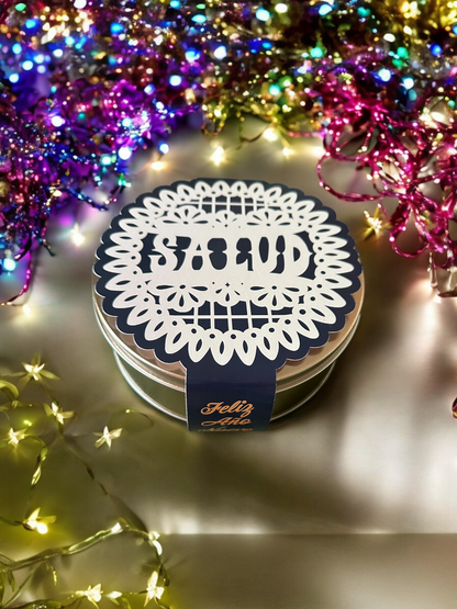 front view of 'salud' paper band wrapped around a cookie tin with party confetti around the tin
