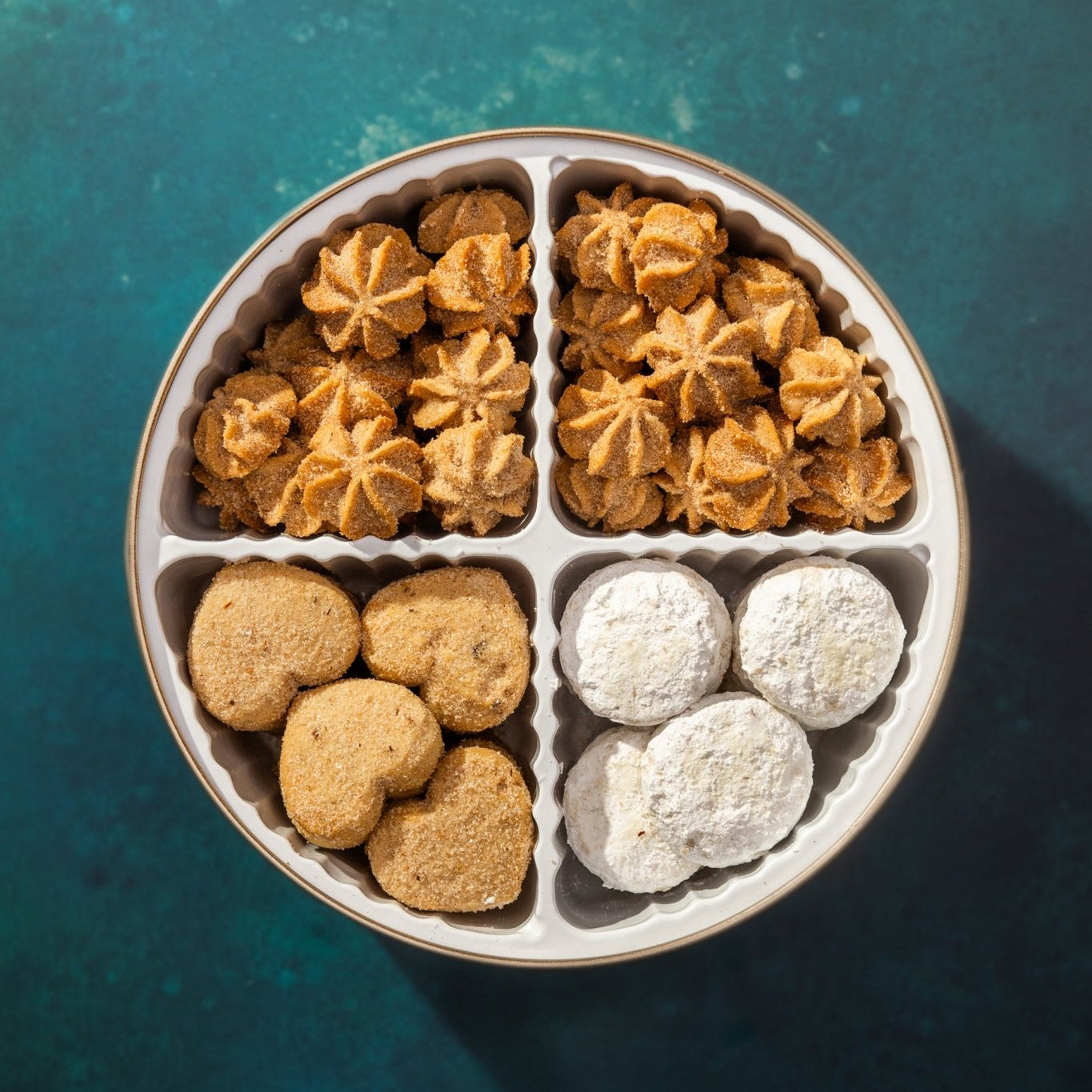 4 cavity cookie tin with three types of mexican cookies against a dark green background
