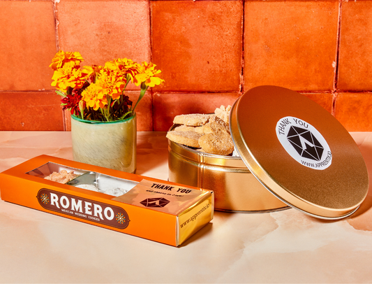 Romero packaging with a gold tin and flowers on a textured surface