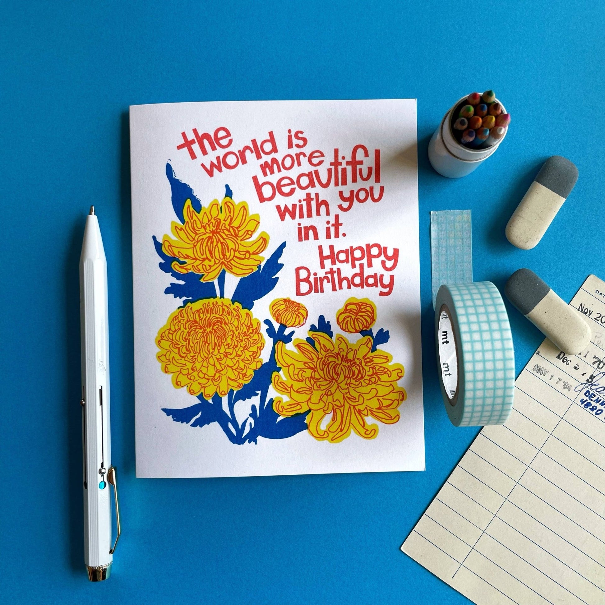 Greeting card with floral design and birthday message on a blue background with stationery items.