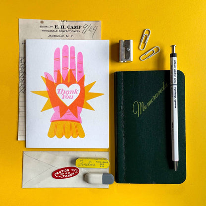 Stationery items including a card, notebook, pen, and paper clips on a yellow background