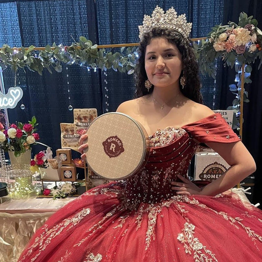 Woman in a red quinceañera dress holding a tambourine, with a decorated backdrop.