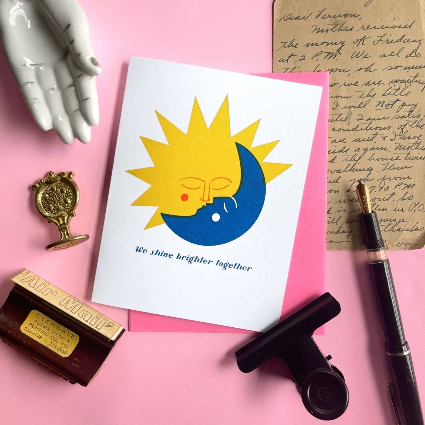 Card with sun and moon design on pink surface with stationery items